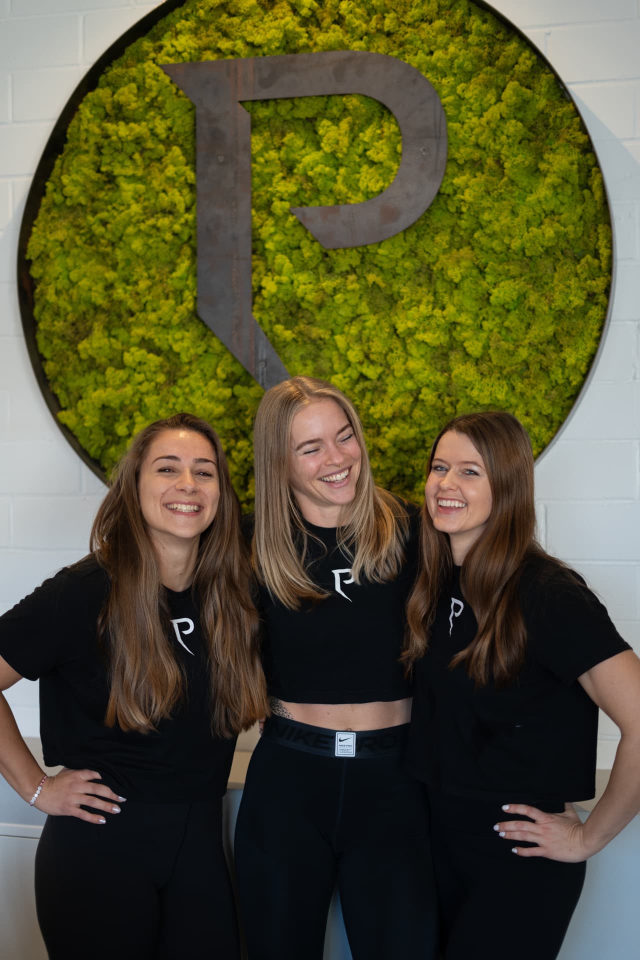Caro, Insa und Tina, die drei Gründerinnen des Peak Women's Club, vor der Moos-Logowand